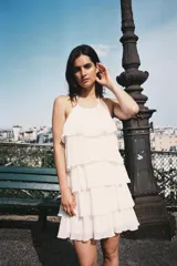Minivestido blanco con cuello halter ajustable con lazos y falda escalonada con volantes. Espalda descubierta.