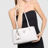 Cartera tote Guess modelo Meridian, color blanco con textura granulada y detalles metálicos dorados. Incluye llavero colgante con logo de la marca.