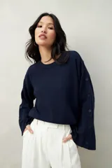 Sweater color beige de tejido de punto, con cuello redondo y mangas largas acampanadas con botones decorativos en los laterales.