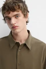 Camisa negra relaxed fit confeccionada en tejido fluido con mezcla de viscosa. Tiene cuello solapa, manga larga con puño abotonado y cierre frontal con botones.