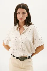 Camisa blanca con estampado de lunares negros, de corte clásico, manga corta y cuello camisero.