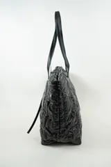 Bolso tipo shopper acolchado color gris metalizado, con cierre superior y doble asa de hombro en color gris claro.
