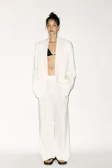 Blazer blanco de corte oversize, con cuello solapa, manga larga con hombreras, bolsillos de doble vivo en el delantero, aberturas en la espalda y cierre cruzado con botones.