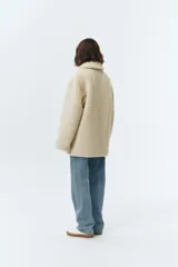 Chaqueta reversible de cuero sintético color marrón con forro de corderito sintético blanco. Presenta cuello de solapa, cierre frontal con botones, bolsillos de parche y detalles de corderito en puños, bolsillos y bordes.