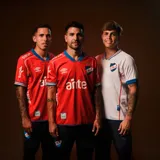 Camiseta de fútbol Umbro del Club Nacional de Football, modelo Away 1 2025. Diseño rojo con detalles en azul en cuello y mangas. Incluye logo de Umbro, escudo del club y sponsors en el frente.