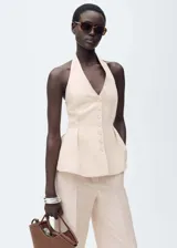 Chaleco color beige con cuello halter y cierre frontal con botones. Diseño con peplum y corte entallado.
