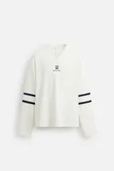 Camiseta blanca de manga larga con cuello en pico y corte relaxed fit. Presenta un estampado con el número 12 y dos rayas horizontales en color azul marino en ambas mangas.