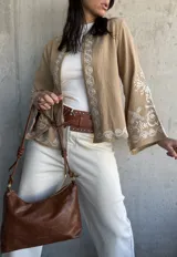Chaqueta color beige con bordados blancos en el frente y las mangas, de corte recto y mangas anchas.