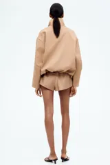 Campera color beige de sarga con cuello, cierre oculto adelante y bolsillos laterales con cierre. Modelo de corte holgado con pinzas en los codos para dar forma y cordón para ajustar elástico con topes en el bajo. Sin forrar.