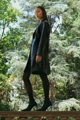 Blazer negro de eco cuero con solapas, cierre de botón frontal y pespuntes blancos en los bordes.