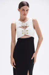 Vestido midi negro y blanco, sin mangas, con top blanco drapeado con bordados florales de tul con perlas y cuentas de vidrio doradas, falda negra con tajo lateral y corte ajustado.