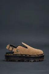 Mules de cuero color camel, estilo zueco cerrado con abertura en el empeine, suela plataforma negra gruesa con costura amarilla visible y tira ajustable con hebilla en el talón.