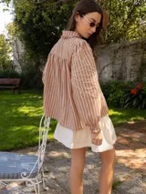 Camisa de denim azul con cuello camisero con volados, mangas largas abullonadas con puños elastizados y bordado blanco en las mangas.