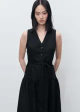 Vestido midi negro sin mangas, confeccionado en lino. Presenta escote en V, cierre frontal con botones y cinturón de lazo. La falda es acampanada con un volante en el ruedo.