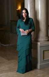 Vestido largo de fiesta color verde oscuro, con mangas acampanadas y falda con volados en cascada. Incluye clutch plateado.