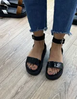 Sandalias negras con plataforma track y tira ancha sobre los dedos. Presentan una tira con hebilla alrededor del tobillo.