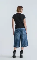 Bermuda larga de denim azul con lavado ácido y efecto desgastado. Presenta un calce oversize, talle alto con cinturón de tela a juego y ruedos deshilachados.