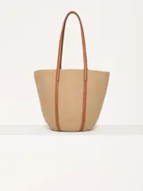 Bolso tote de hilo color beige con estructura firme y diseño espacioso. Tiene correas largas de cuero vacuno color marrón para llevar al hombro, aplique frontal de limón y logo metálico JCH.