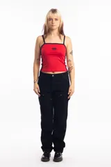 Top deportivo rojo con breteles finos y ribete negro, con logo ovalado en el pecho y dos líneas verticales negras en los laterales.