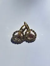 Aros dorados con dije circular de resina y strass, con flor de vidrio verde en el interior. El arito es de acero quirúrgico.