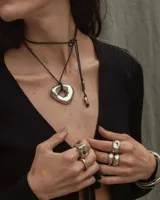 Collar con dije dorado irregular con agujero central, colgando de cordón negro ajustable.