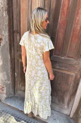 Vestido largo estampado con flores blancas sobre fondo dorado, con mangas cortas con volados y escote en V.