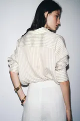 Camisa de manga larga con cuello solapa, a rayas verticales grises y blancas. Tiene un bolsillo de plastrón en el delantero y cierre frontal con botones.