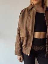 Campera marrón de gamuza con cuello clásico, cierre frontal con cremallera y bolsillos con solapa y botón.