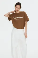 Remera color marrón con estampado blanco con la frase 'Los Ángeles California'. Corte recto y holgado, mangas cortas y cuello redondo.