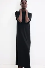 Vestido largo negro de punto suave, corte recto, cuello redondo, mangas cortas y tajo lateral pronunciado.