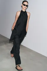 Top negro satinado con cuello halter, manga sisa y bajo asimétrico. Cierre en la espalda.