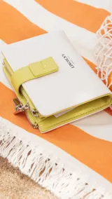 Billetera mediana de símil cuero color blanco hueso con detalles en rojo coral. Posee una presilla de cierre en la parte frontal y cierres de cremallera visibles en el borde superior.