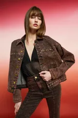 Campera de jean negra de corte holgado con detalles de tachas plateadas en costuras, hombros y puños, y bordado floral blanco en las mangas.