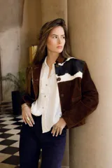 Chaqueta marrón de cuero vacuno con canesú delantero y trasero en cuero vacuno raza Holando (blanco con manchas negras), con cuello clásico, cierre frontal con botones y bolsillos laterales.
