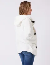 Campera tipo teddy de textura suave y esponjosa en color blanco, con cierre frontal mediante botones y detalles de apliques en cuero sintético negro en la solapa. Presenta bolsillos frontales y un diseño cómodo y abrigado.