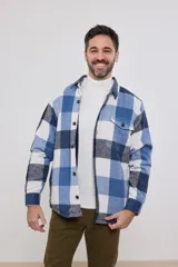 Sobrecamisa de hombre con diseño a cuadros en tonos marrón, beige y blanco. Confeccionada en tejido peludito suave, con cuello clásico, cierre frontal con botones, bolsillo superior y mangas largas con puños abotonados.