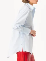 Camisa celeste de poplin, corte clásico, largo a la cadera y mangas largas. Cuello con detalle de piedras engarzadas. Cierre frontal con botones de pasta al tono.