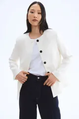Blazer entallado color blanco con cuello redondo, cierre frontal con un botón visible y tapeta con botones ocultos. Tiene bolsillos delanteros ribeteados, abertura en los puños y pinzas moldeadoras adelante y atrás. Está forrado.