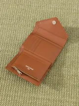Billetera pequeña color visón, con solapa y cierre a presión. Diseño acolchado con pespuntes en forma de V y logo metálico con forma de labios.