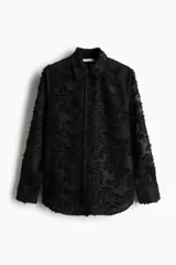Camisa negra con textura, cuello de pico, botones delanteros, canesú con pliegues en la espalda, mangas largas con hombros caídos, puños abotonados y bajo redondeado.