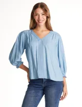 Blusa de lyocell color azul claro, con escote en V, detalles de costuras verticales en el frente y mangas tres cuartos con puños elastizados.