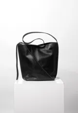 Bolso bucket negro de cuero con costuras diagonales en el frente, doble asa de hombro y cierre con broche imán. Interior forrado en algodón con bolsillo con cierre y bolsillo abierto.