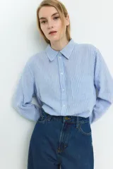 Camisa celeste y blanca a rayas verticales, confeccionada en mezcla de lino y viscosa. Tiene cuello clásico, botones frontales, bolsillo de parche en el pecho, mangas largas con puños abotonados y bajo redondeado.