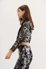 Blazer negro de terciopelo con estampado floral plateado, corte cropped y mangas largas.