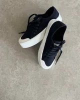 Zapatillas urbanas de lona color negro con plataforma blanca y cordones negros.