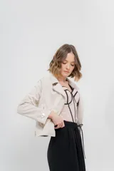 Chaqueta color beige de tela tipo gamuza con elastano, cuello solapa, manga larga con trabillas en hombro, bolsillos delanteros con cremallera metálica y cierre frontal con cremallera.