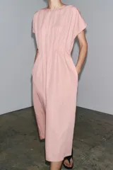 Vestido midi color marrón confeccionado en hilatura con mezcla de algodón y lino. Tiene cuello redondo, manga corta caída y detalle de pliegues en la cintura. Cierre en la espalda con abertura y botón.