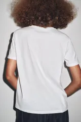 Camiseta blanca de corte recto y manga corta, con estampado frontal de una fotografía en blanco y negro y texto "Amsterdam 74".