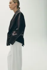 Blazer marrón oscuro de efecto piel, con cuello solapa y manga larga. Tiene bolsillos de plastrón en la parte delantera, forro interior a tono y cierre frontal con botones.