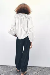 Camisa blanca de cuello redondo y manga larga con bordados combinados a tono y cierre frontal con botones.